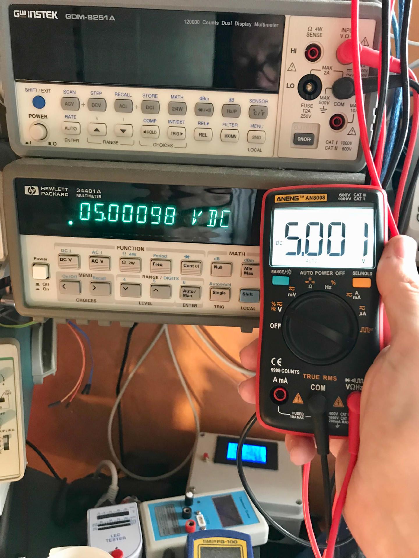 The AN8008 reading 5.001 V against the HP 34401A&rsquo;s 5.00098 V DC, with a GW Instek GDM-8251A on the shelf above