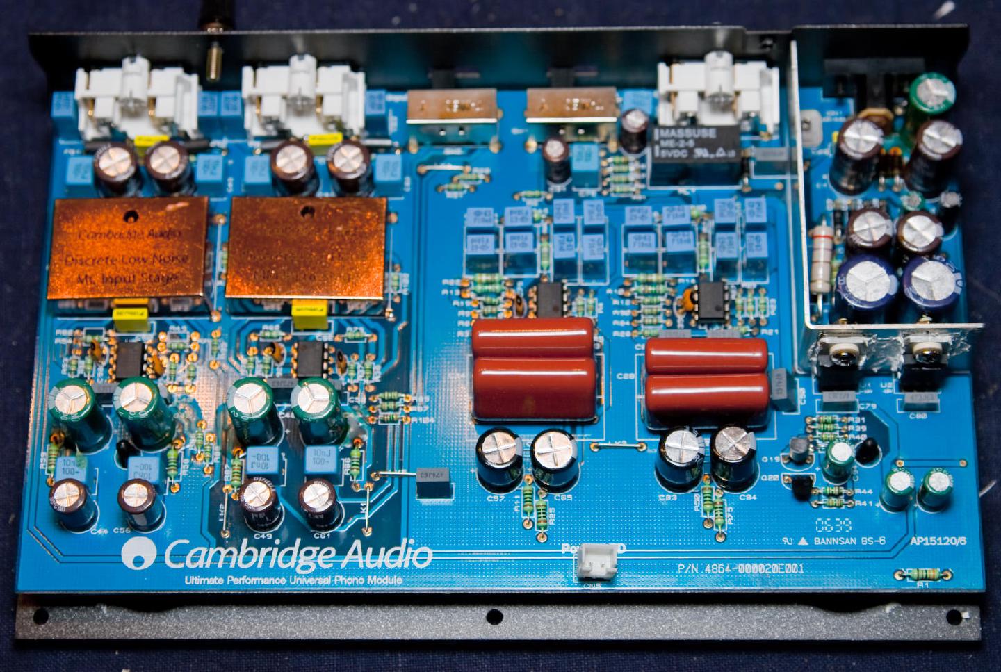 The full Cambridge Audio phono module board, its two copper-shielded input stages at the left and rows of red film capacitors across the middle