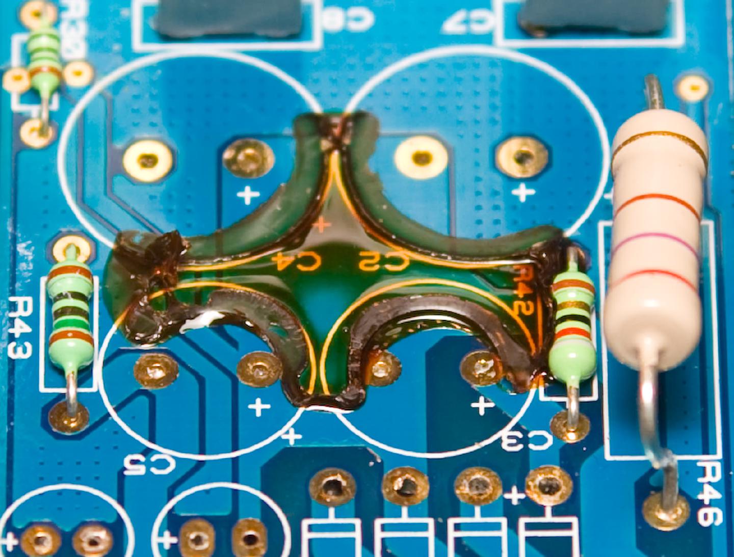 Close-up of the C2 to C5 pads where the removed capacitors were bridged with wire and sealed under a lump of dark adhesive