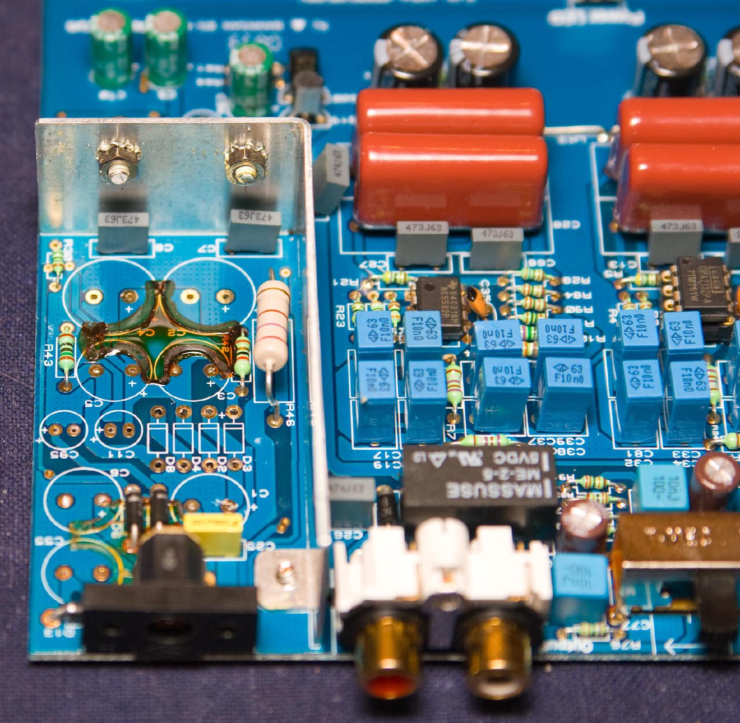 The board at an angle, showing the aluminium shield plate beside the reworked capacitor pads and, to the right, an NE5532 and the OPA2132PA