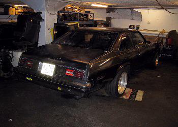The rebuilt black Chevy Nova seen from the rear three-quarter in a garage, sitting low on wide polished wheels
