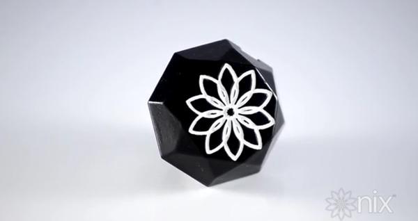 Nix Color Sensor The Nix colour sensor, a small faceted black polygon with a white flower logo on its face