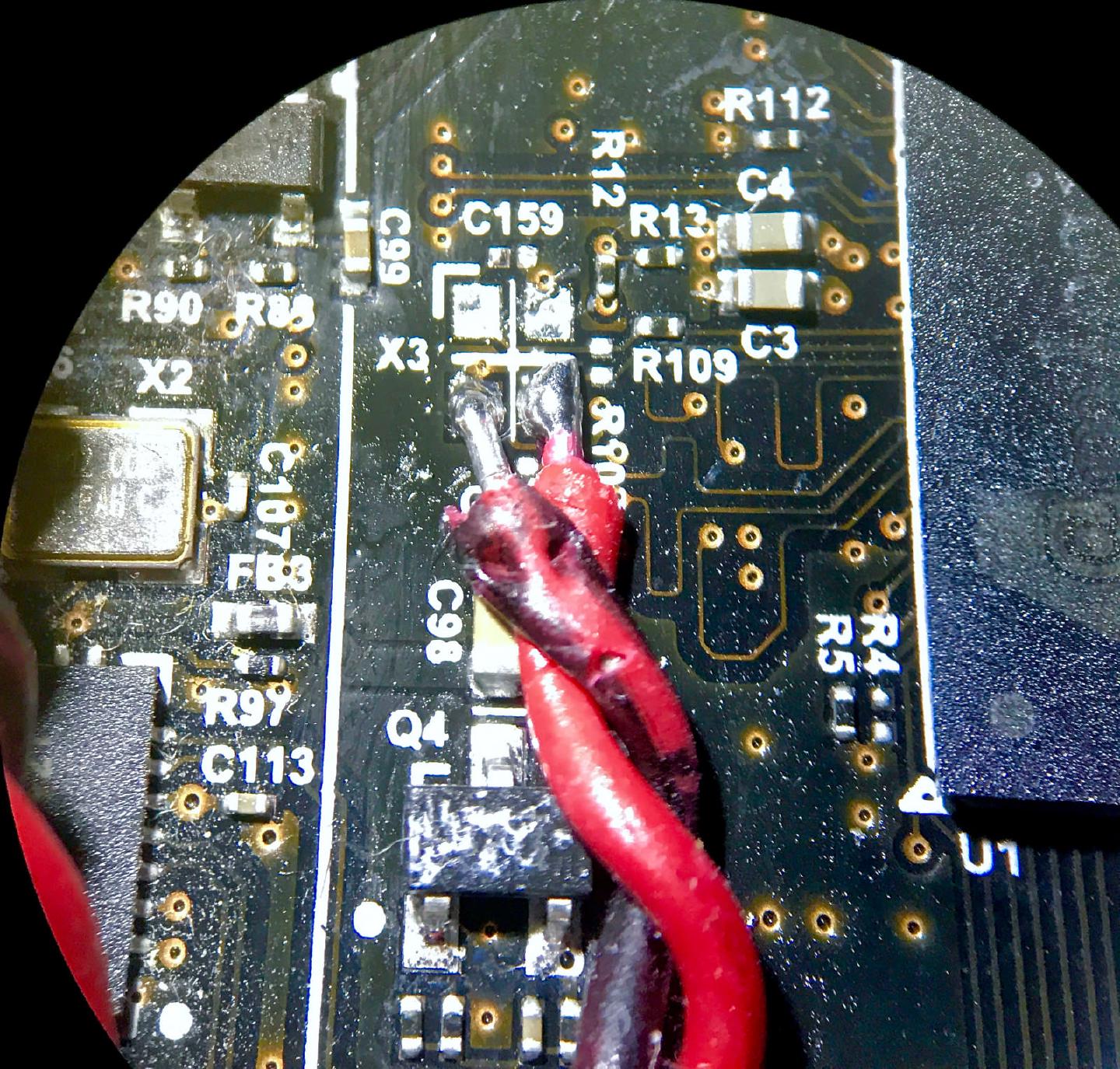 Microscope view of the Odroid C2 board with the X3 crystal removed and two red wires soldered to its pads to feed in an external clock