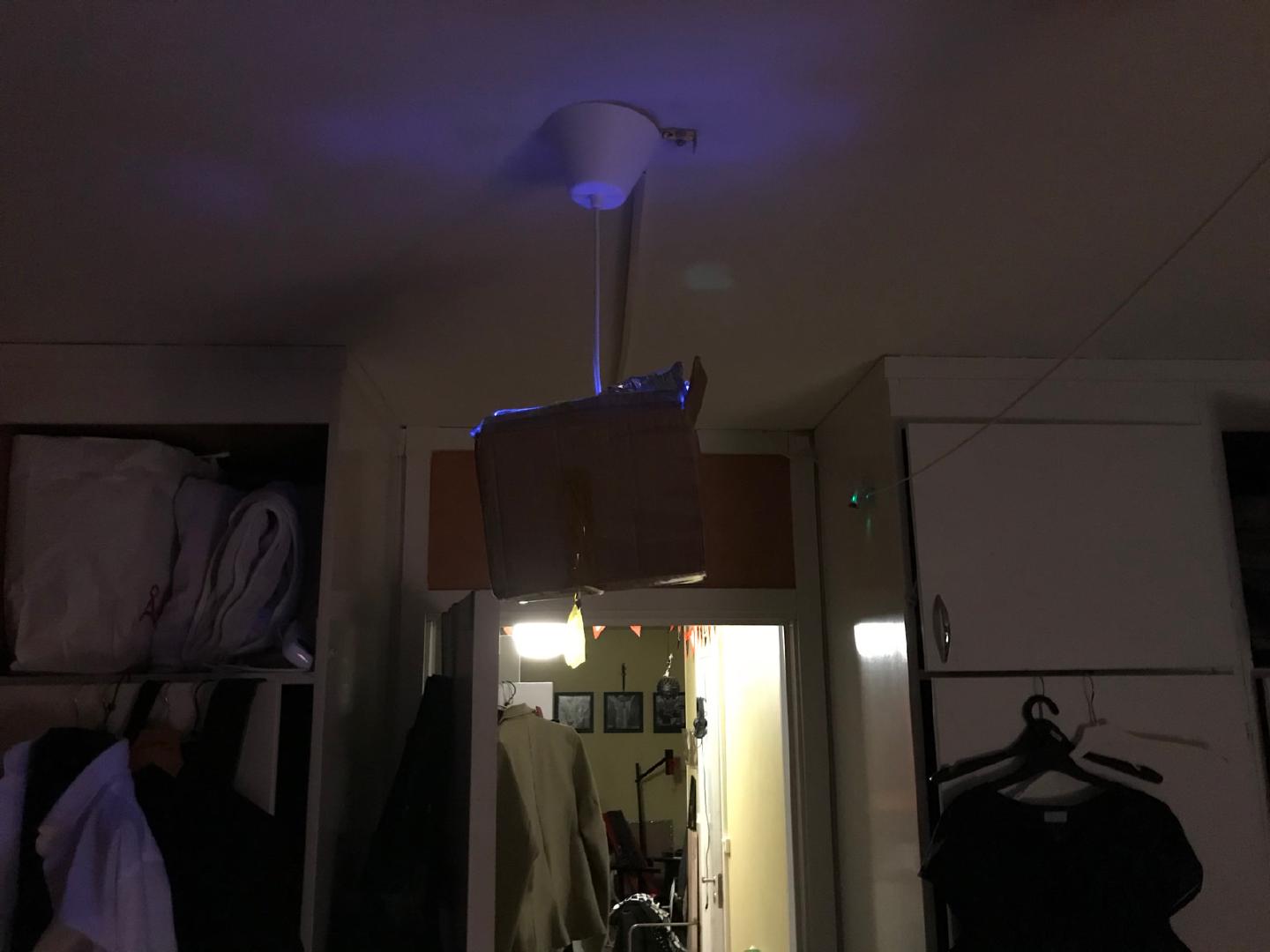 The foil-lined box taped up under a ceiling lamp fitting, the UV bulb inside casting blue light across the bedroom ceiling