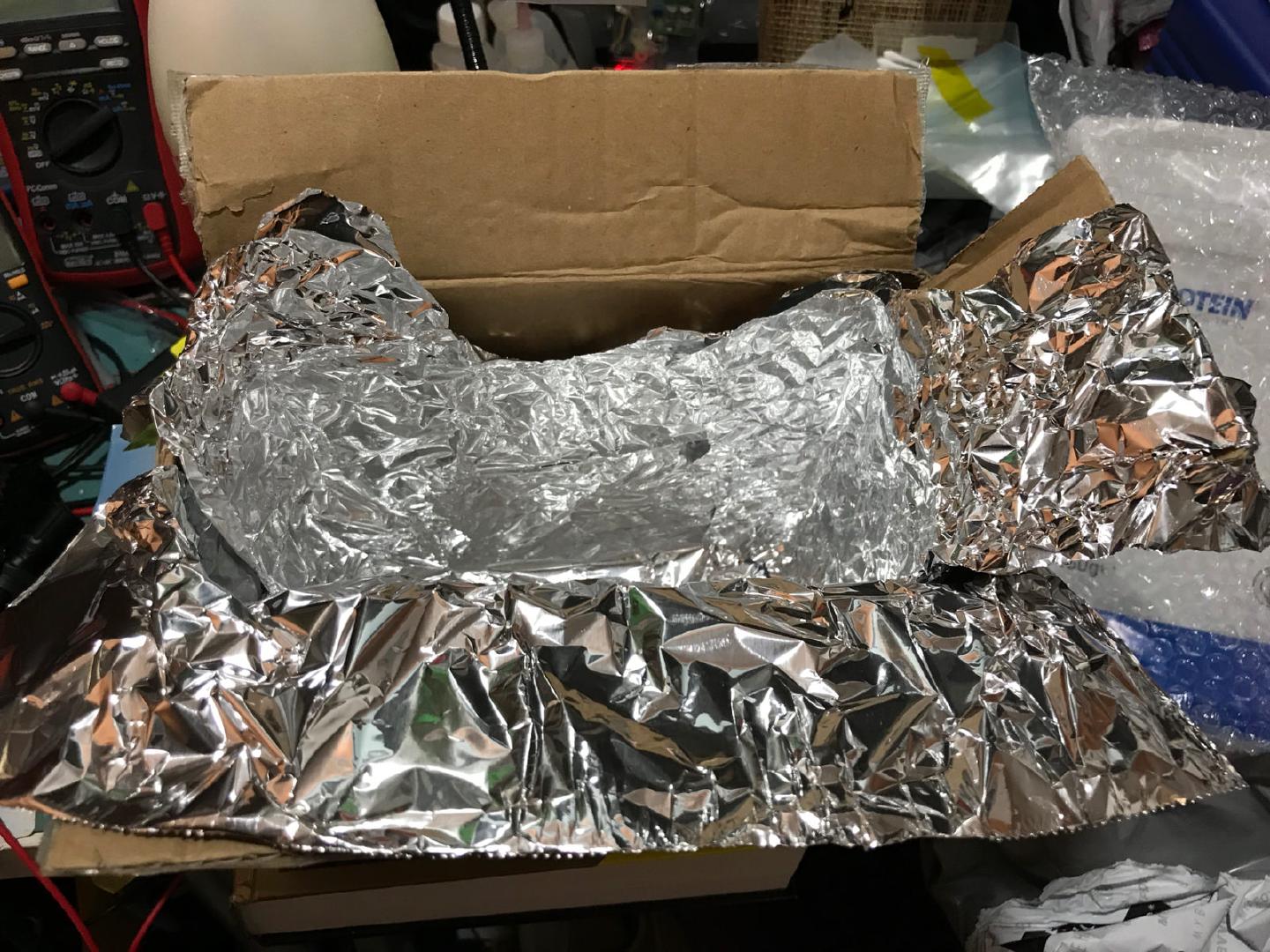 A cardboard box lined with crumpled aluminium foil, improvised as a UV exposure chamber on the workbench
