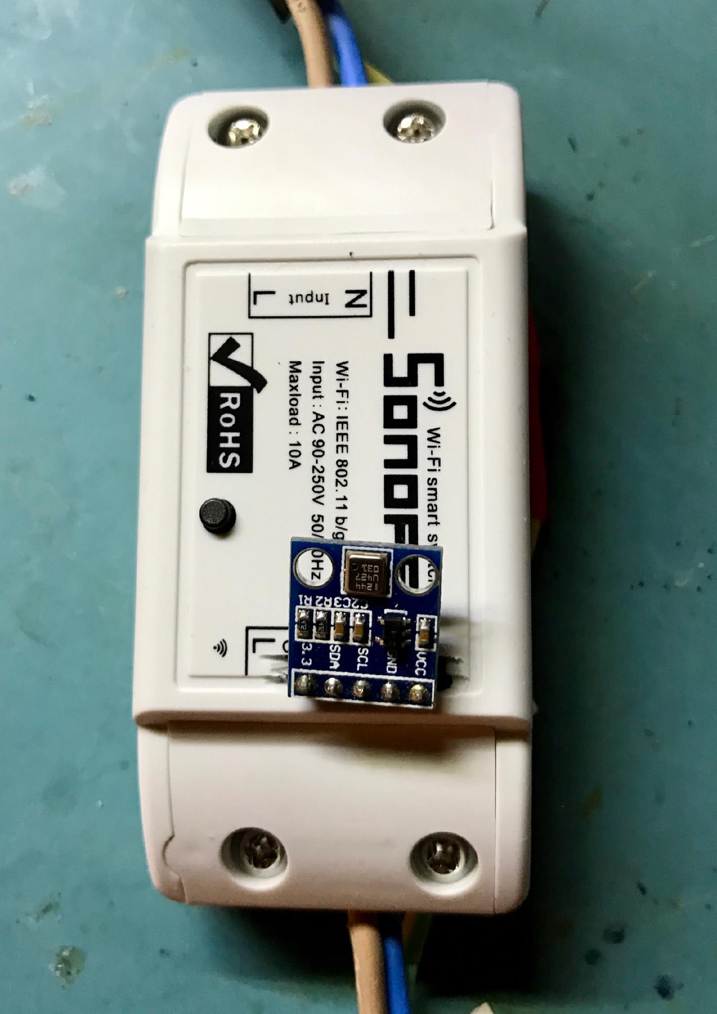 A small blue BMP180 breakout board taped to the front of a Sonoff, its SDA, SCL, GND and VCC pins labelled